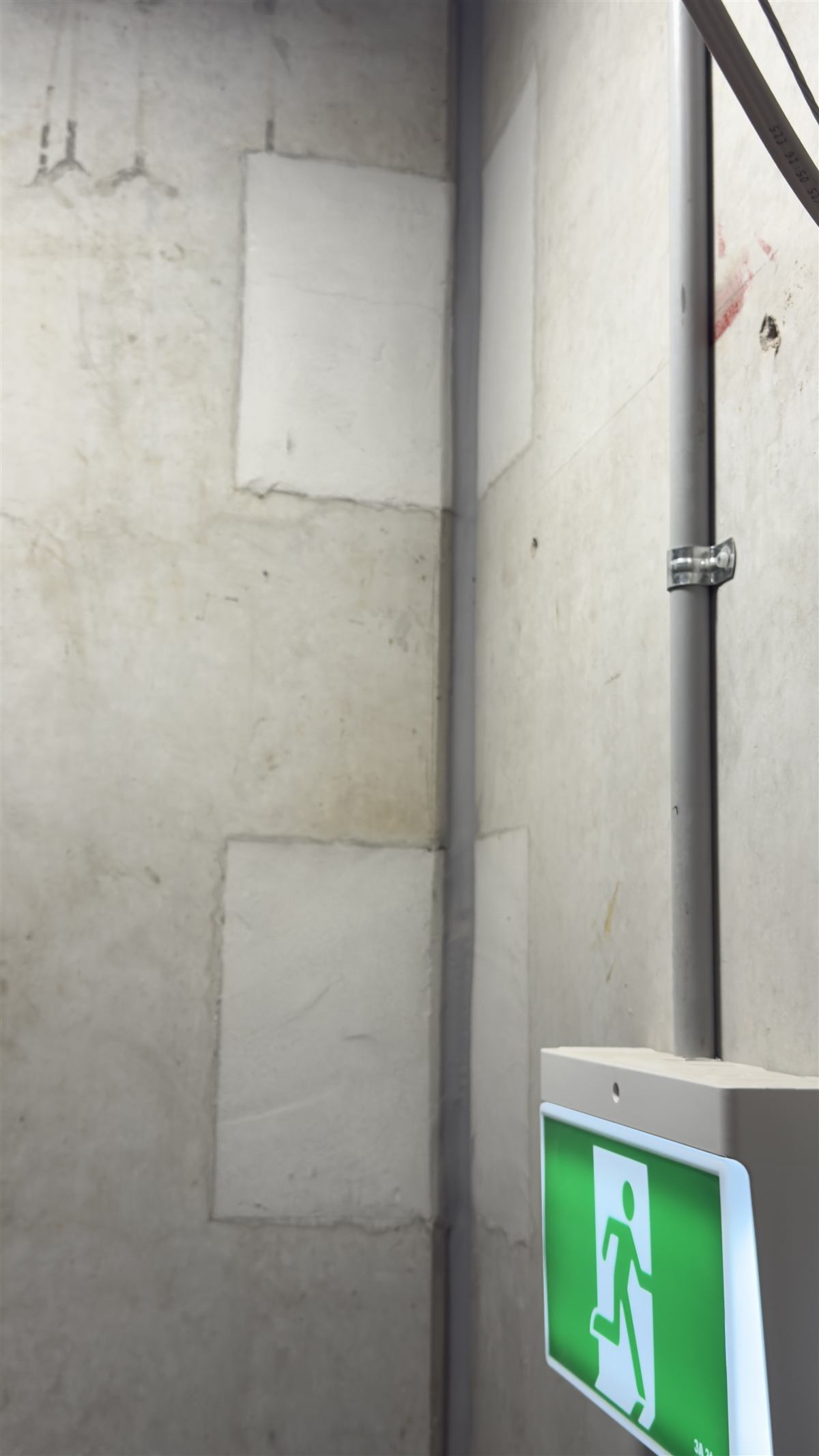Patched wall penetrations beside a fire exit sign